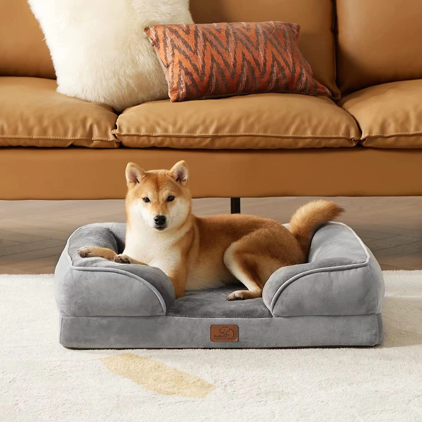 Dog lying on a gray pet bed in a living room with a couch in the background